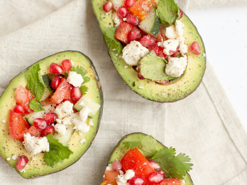 A sliced avocado, a handful of almonds, and a bottle of olive oil, showcasing healthy fats essential for muscle recovery and hormonal balance.